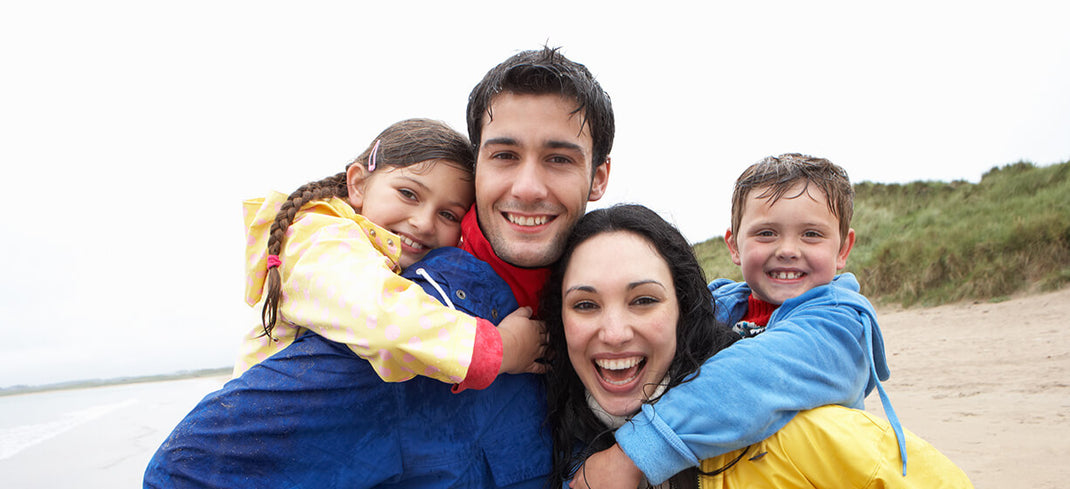 mand and woman carrying a young boy and gitlr on their shoulders outside on a beach